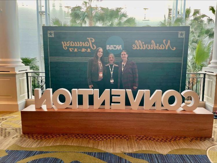 three women standing behind sign hat says Convention